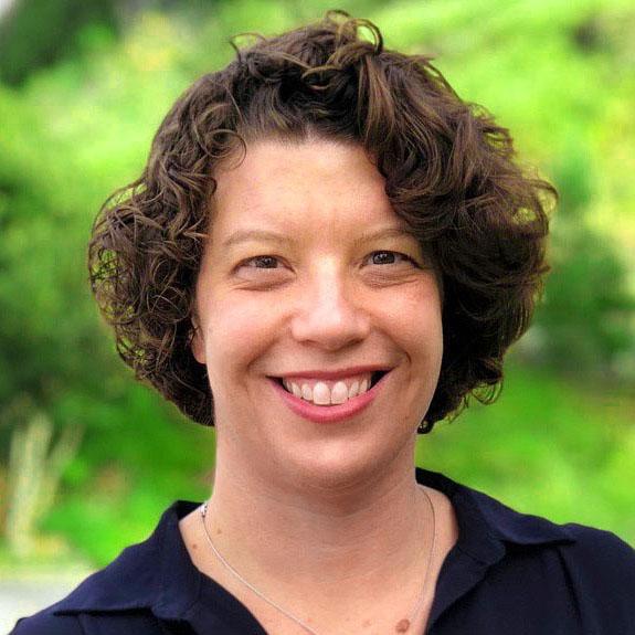 Headshot of Valerie Threlfall, founder and executive director of Listen4Good, in front of greenery.