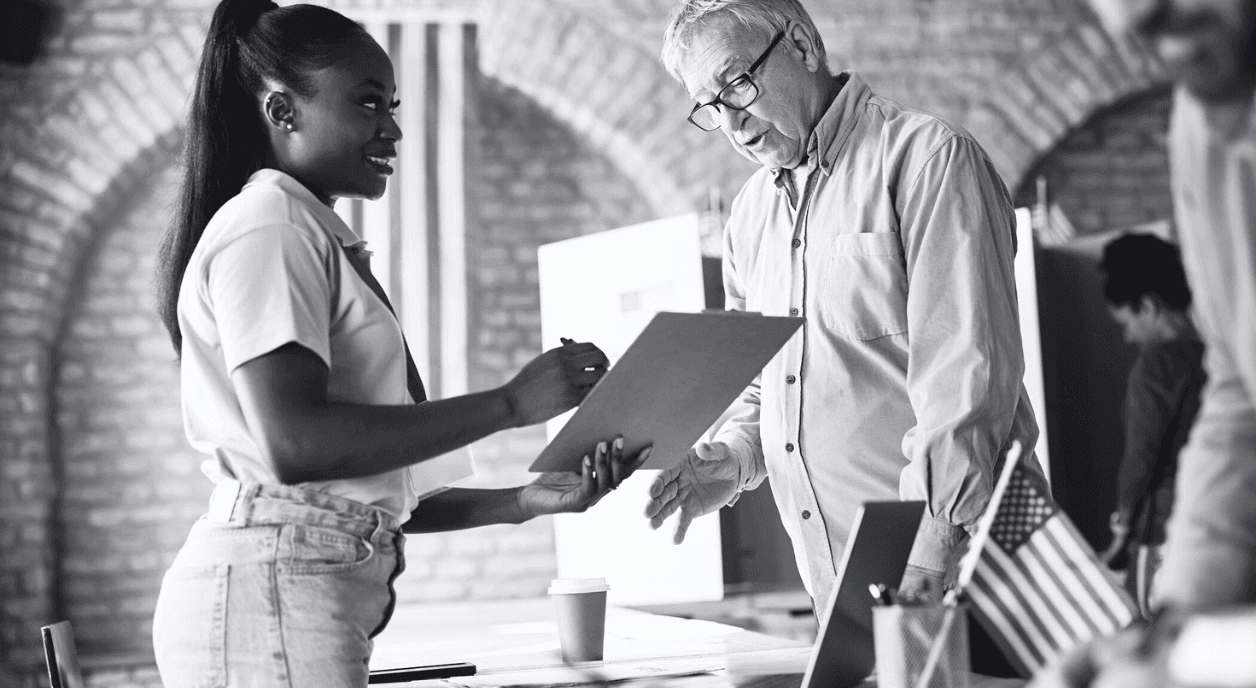 An older man talking to a young Black woman at a voting location.