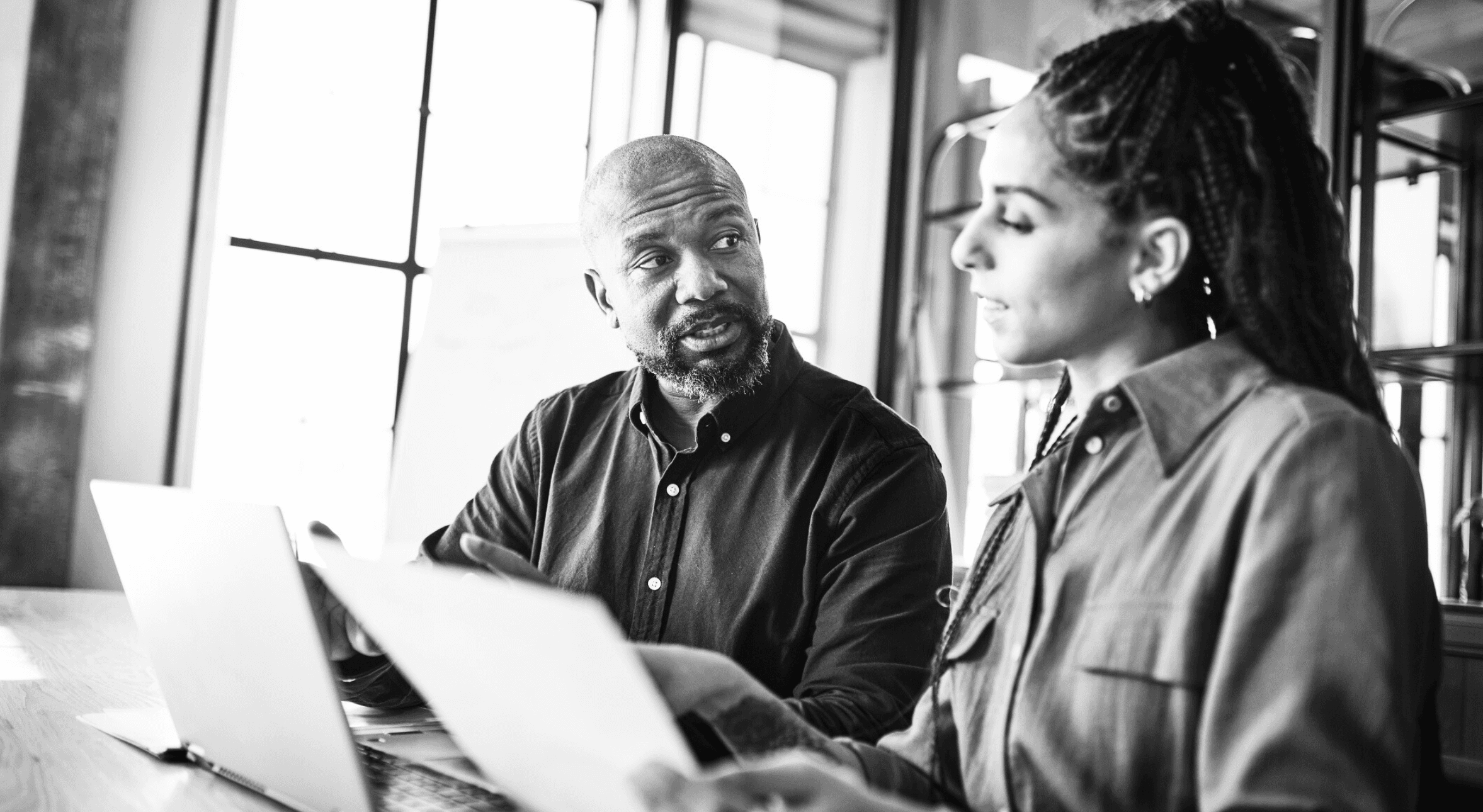 Two colleagues comparing notes on a laptop and piece of paper.