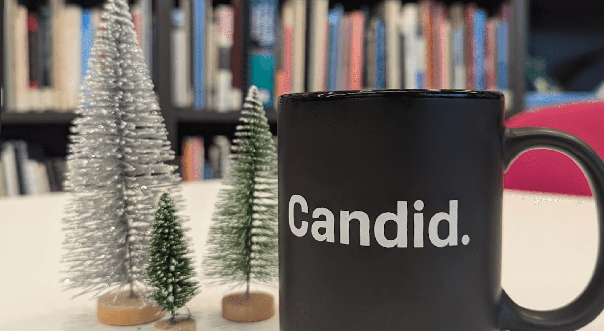 A Candid mug in front of mini Christmas trees.